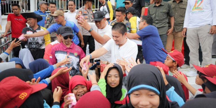 Bupati Kolaka Timur, Abd Azis, membagikan susu kepada para pelajar saat pembukaan O2SN, FLS3N, serta GSI di lapangan sepak bola Desa Gunung Jaya, Kecamatan Dangia, Jumat (11/7/2025). (Foto: Istimewa)
